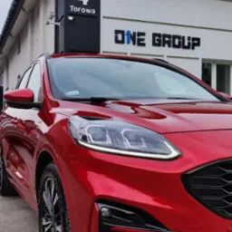 Czerwony samochód Ford Kuga zaparkowany przed budynkiem firmy ONE GROUP z adresem Torowa 4, widok z przodu, lekko z boku.