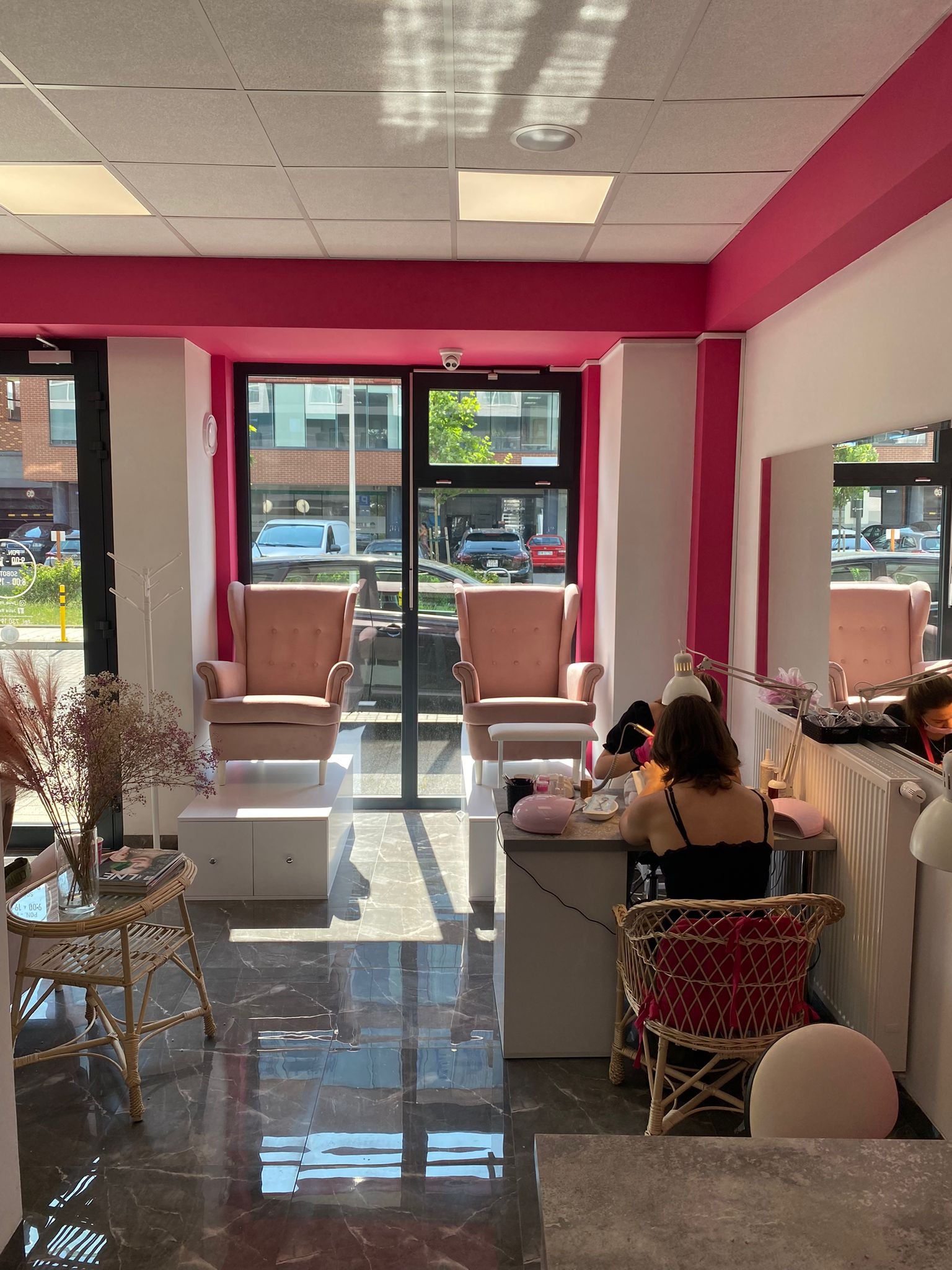 Wnętrze salonu kosmetycznego z fotelem do manicure, oświetleniem punktowym i rattanowym krzesłem dla klientki, jasne ściany z różowymi akcentami.