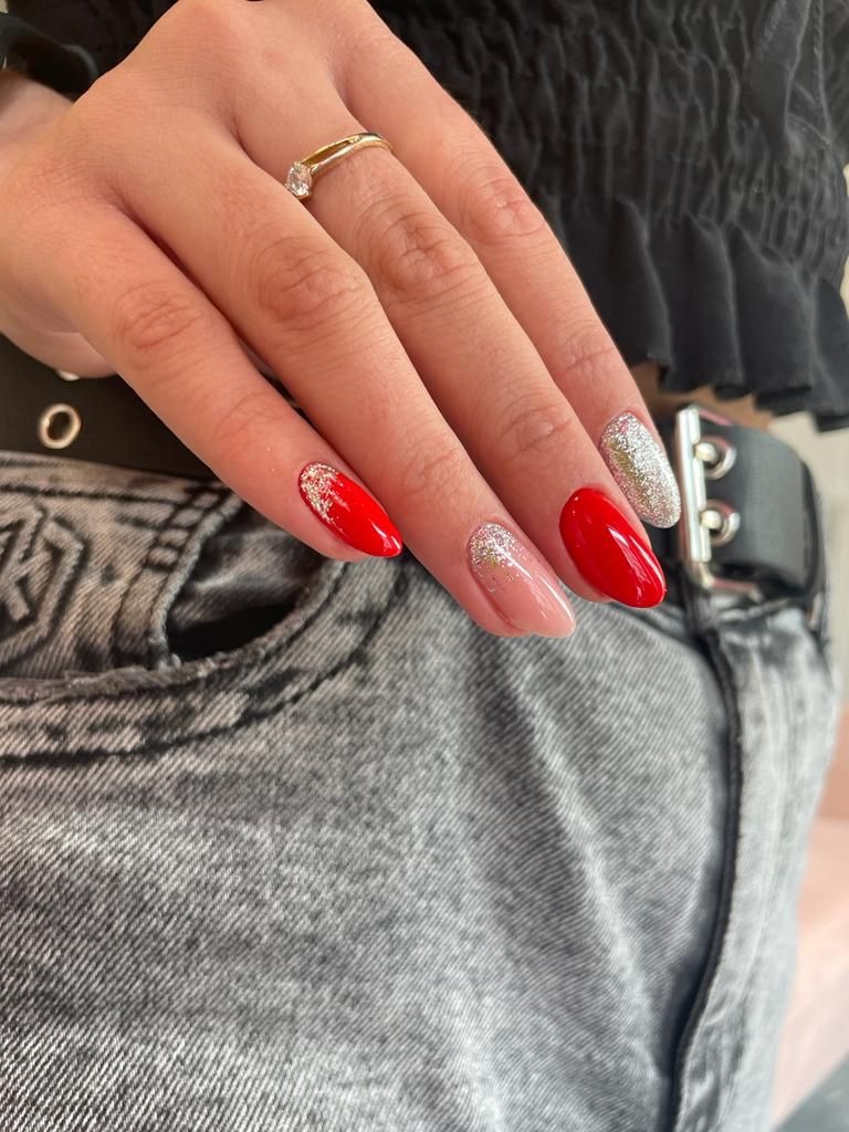 Dłoń z czerwono-srebrnym manicure hybrydowym, pierścionek z brylantem, jeansy z czarnym paskiem w tle.