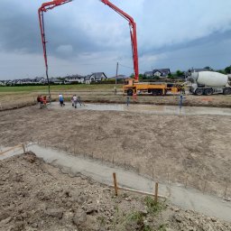 Szerbud - Wylewanie fundamentów pod budowę domu z użyciem pompy do betonu i betoniarki, widoczni pracownicy budowlani.