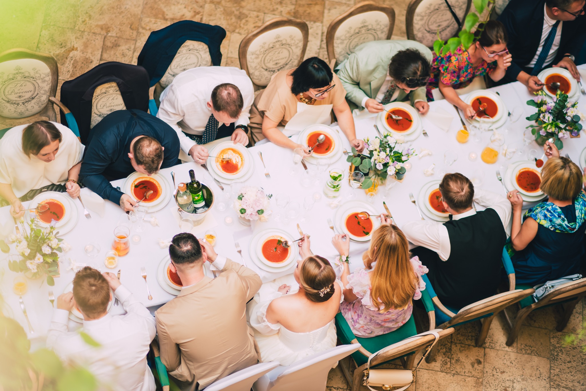 Goście weselni siedzą przy długim stole, jedząc zupę pomidorową podczas przyjęcia weselnego, widok z góry.