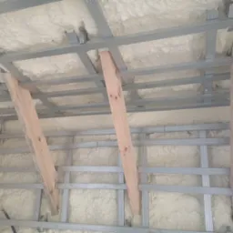 Poddasze w trakcie ocieplania pianką poliuretanową, widoczne drewniane podpory i metalowa konstrukcja szkieletowa.