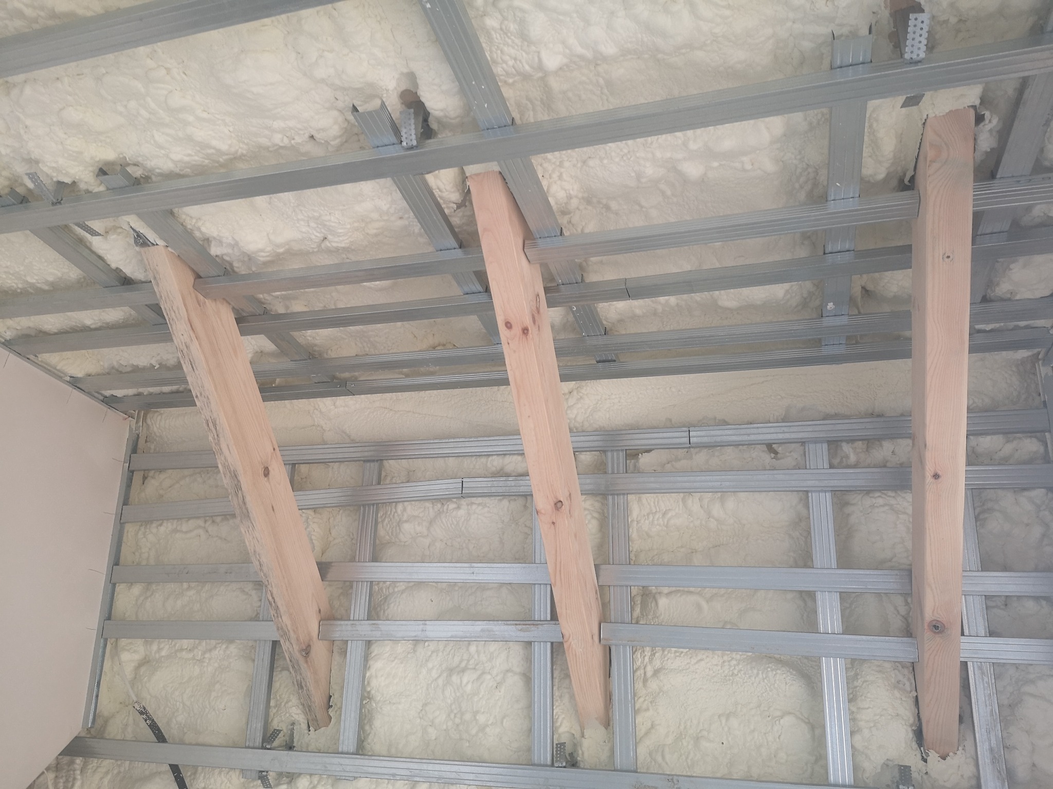 Poddasze w trakcie ocieplania pianką poliuretanową, widoczne drewniane podpory i metalowa konstrukcja szkieletowa.