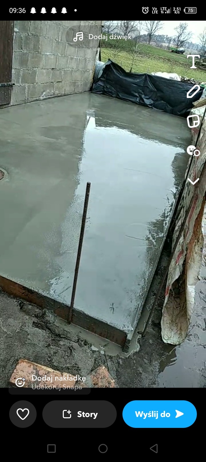 Świeżo wylany fundament z widocznym zbrojeniem w szalunku i murem z bloczków betonowych w tle, przykryty czarną folią.