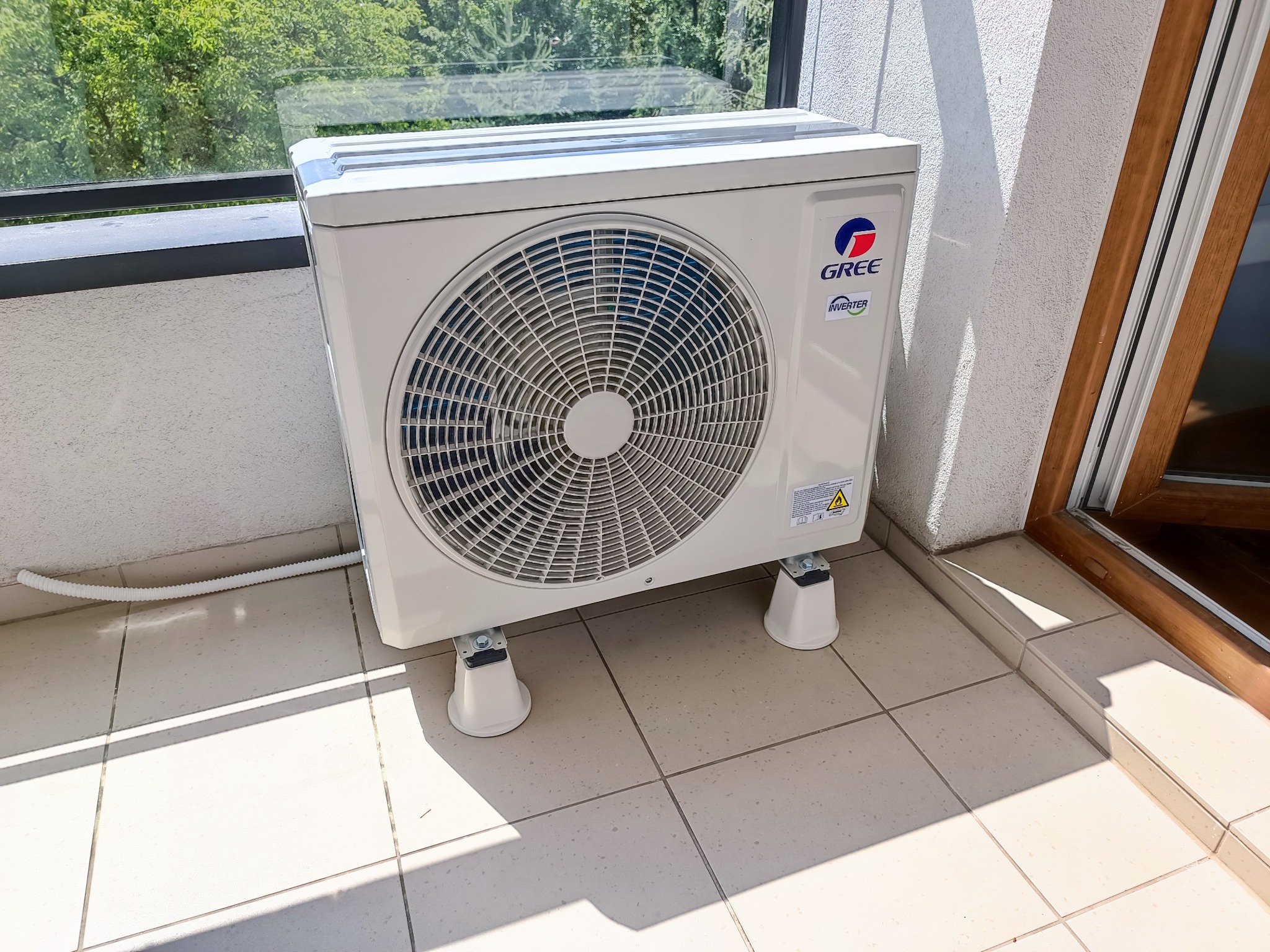 Zewnętrzna jednostka klimatyzacji GREE Inverter zamontowana na balkonie, widoczne białe wsporniki i karbowana rura odprowadzająca skropliny.