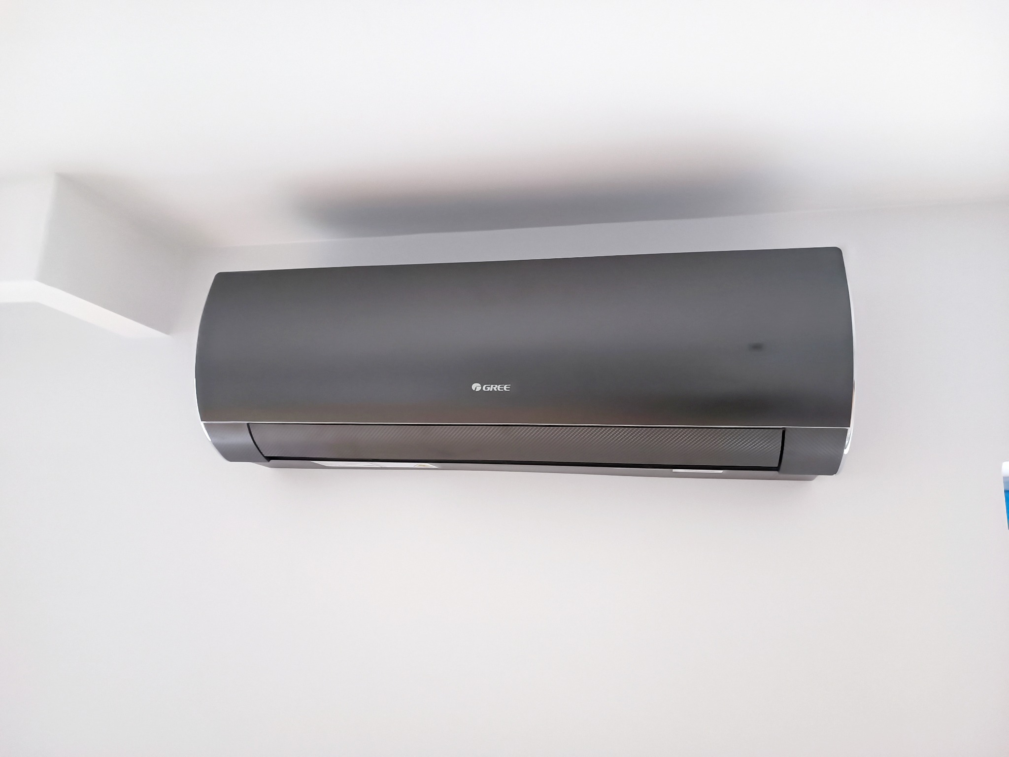 Czarny klimatyzator marki Gree zamontowany na białej ścianie w pomieszczeniu.