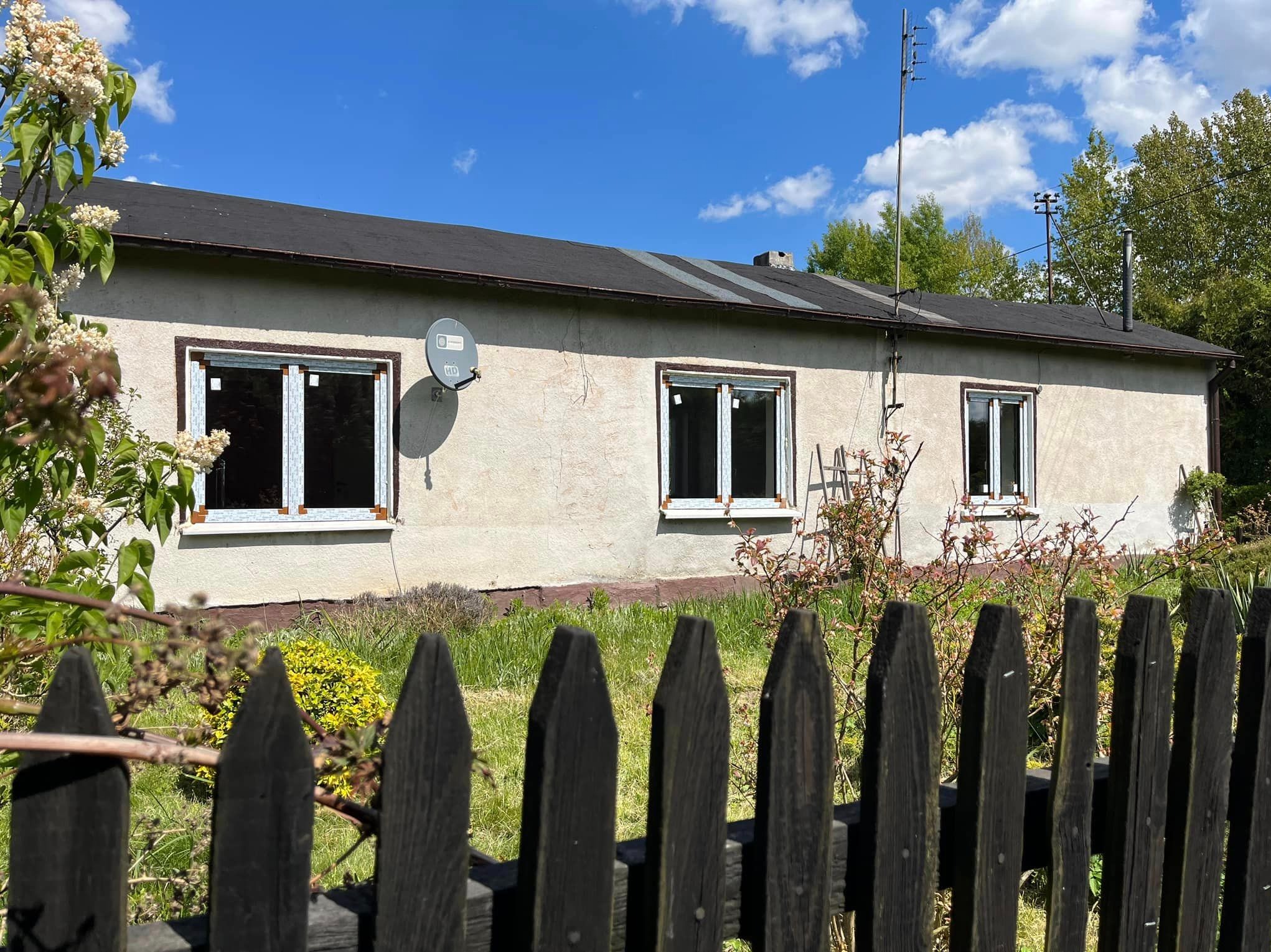 Dom jednorodzinny w Częstochowie z trzema oknami z białymi ramami, widoczny zza drewnianego płotu w słoneczny dzień.