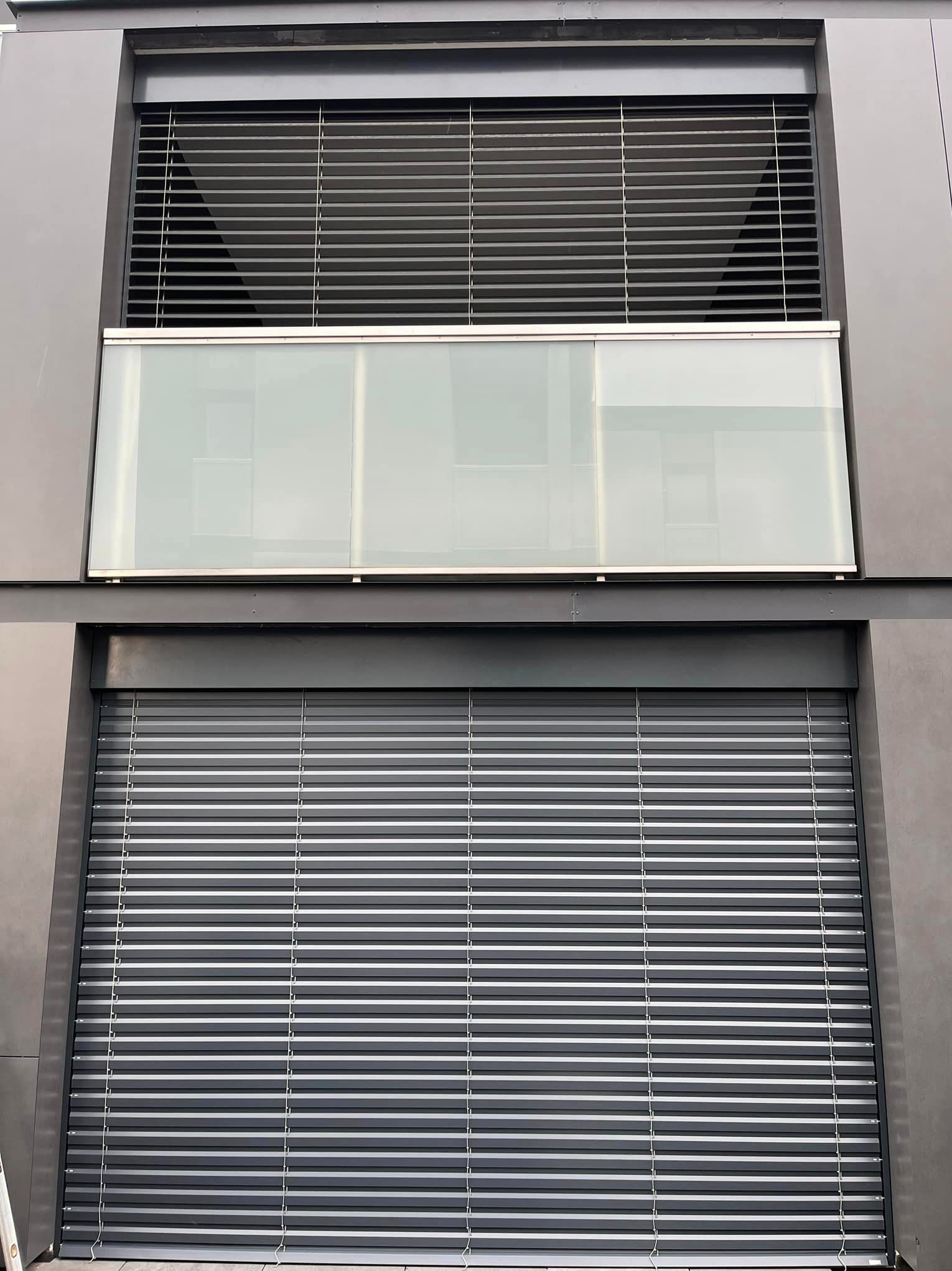 Elewacja budynku z dwoma oknami: górne z żaluzjami fasadowymi w pozycji otwartej, dolne z roletą zewnętrzną całkowicie zasłoniętą.