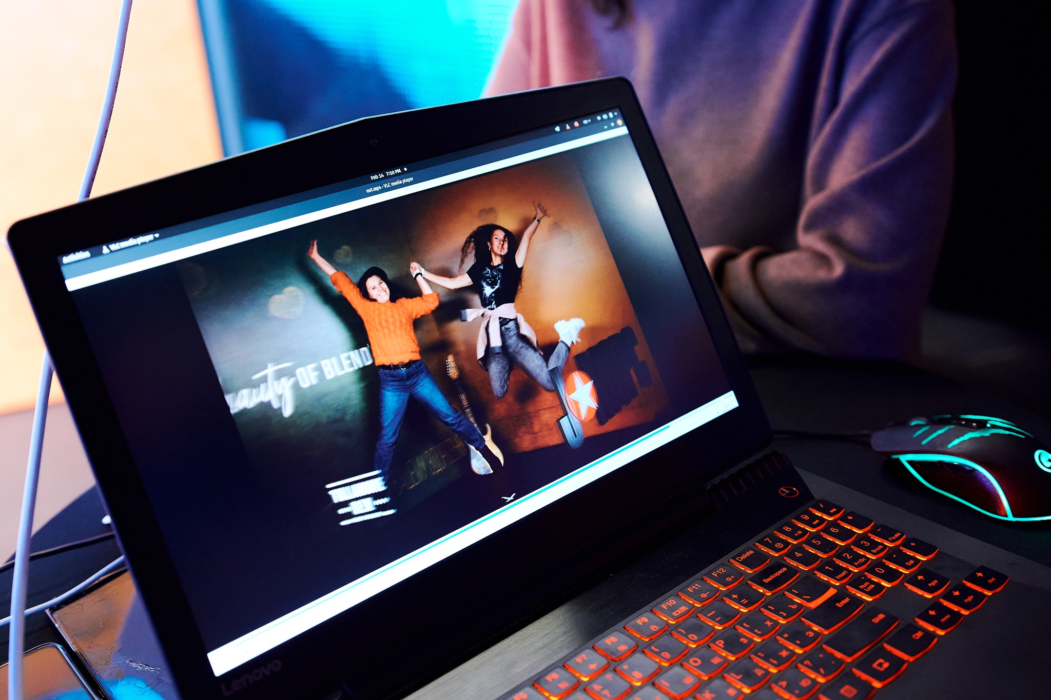 Ekran laptopa Lenovo wyświetla zdjęcie dwóch skaczących osób z gitarami, obok leży gamingowa myszka z podświetleniem.