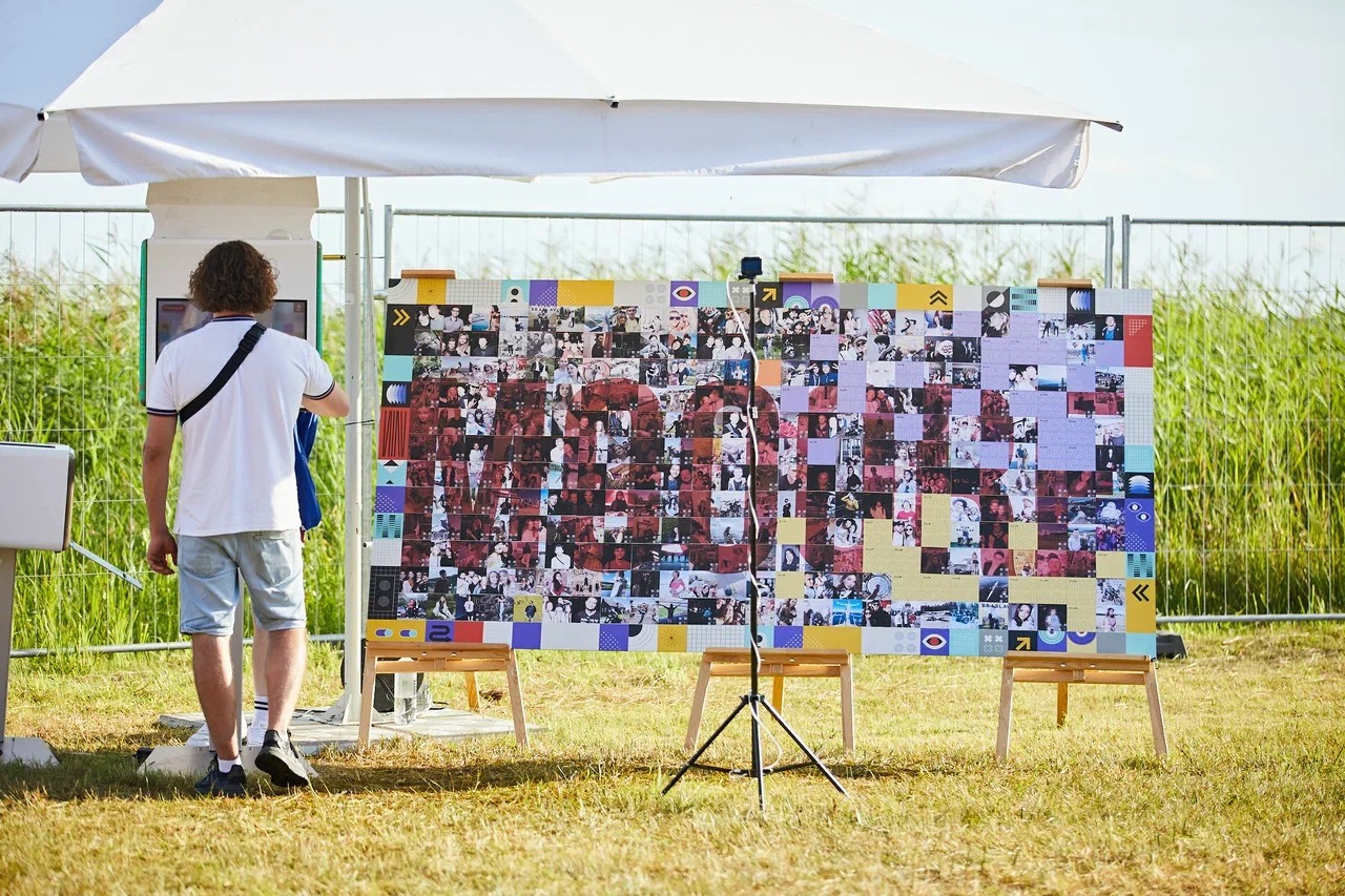 Warszawa: Mężczyzna stoi tyłem do kamery, oglądając mozaikę zdjęć z fotobudki, tworzących napis, umieszczoną na sztalugach podczas plenerowego eventu pod białym namiotem.