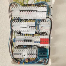 Rozdzielnica elektryczna z zainstalowanymi bezpiecznikami, zabezpieczeniami przepięciowymi i przewodami, uzupełniona o narzędzia na podłodze: taśma izolacyjna, nóż, szczypce, kombinerki.