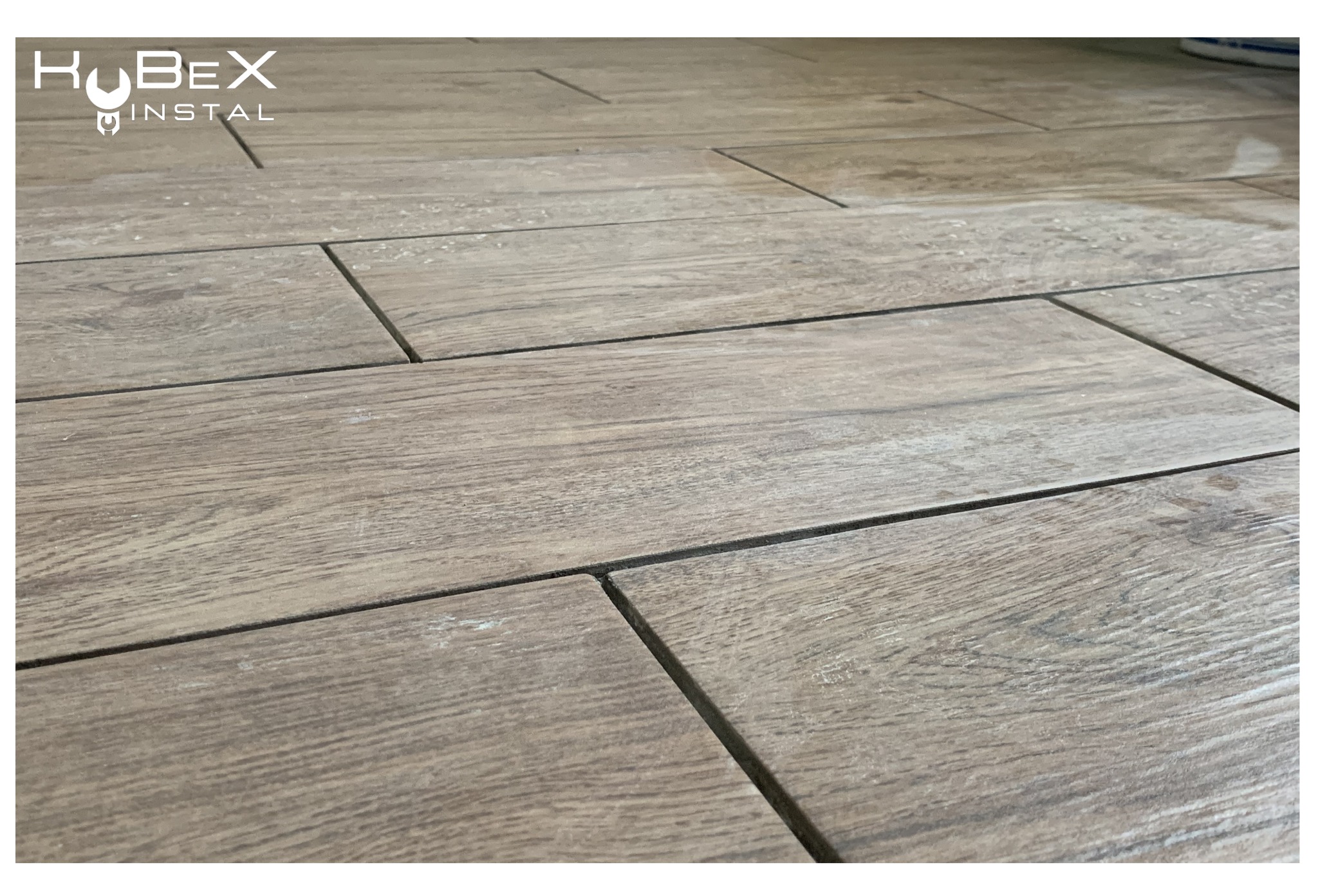 Ułożona podłoga z płytek imitujących drewno w Słowiku, widoczne fugi i logo firmy instalacyjnej w rogu.