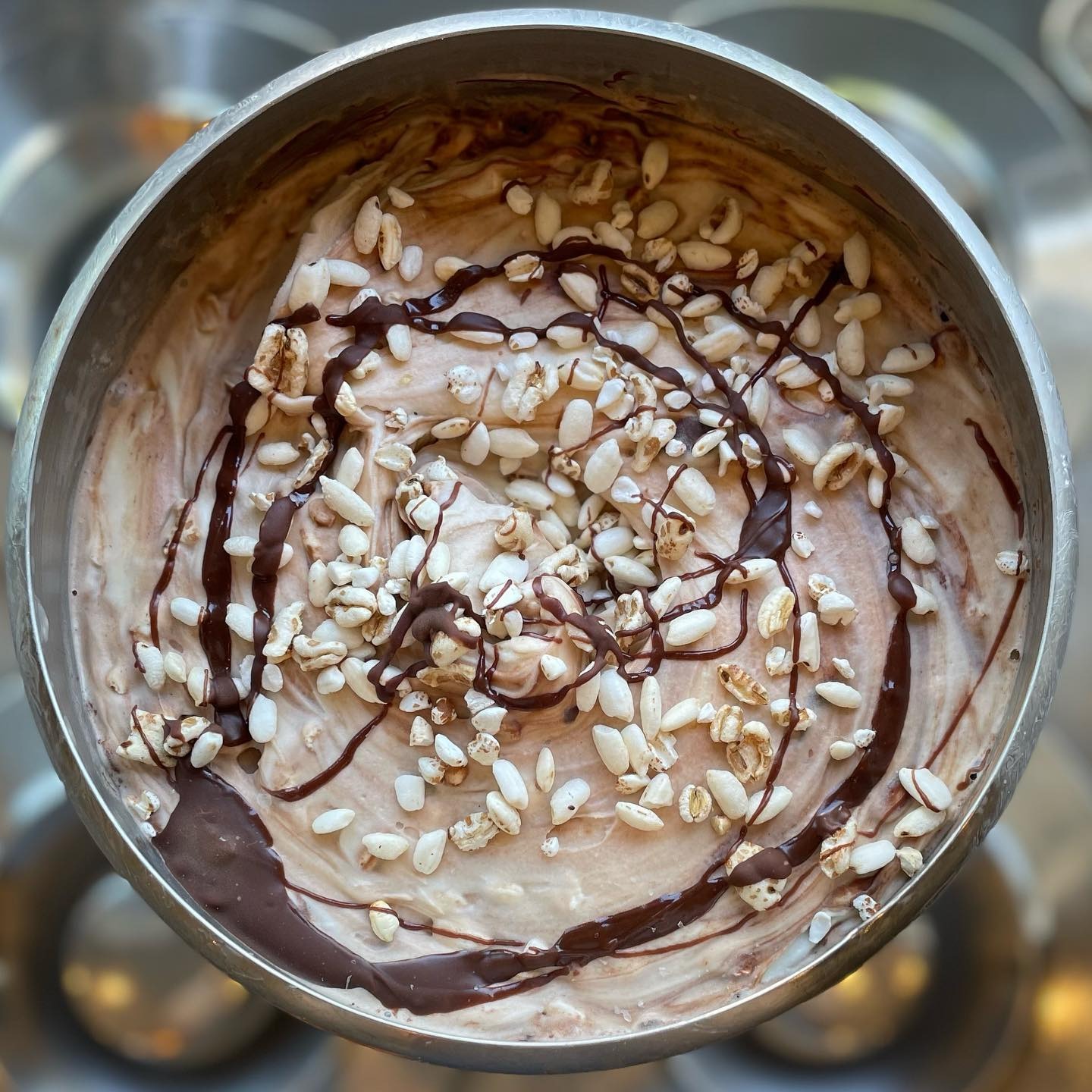 Deser lodowy w metalowej misce, polany czekoladą i posypany ekspandowanym ryżem, widok z góry.