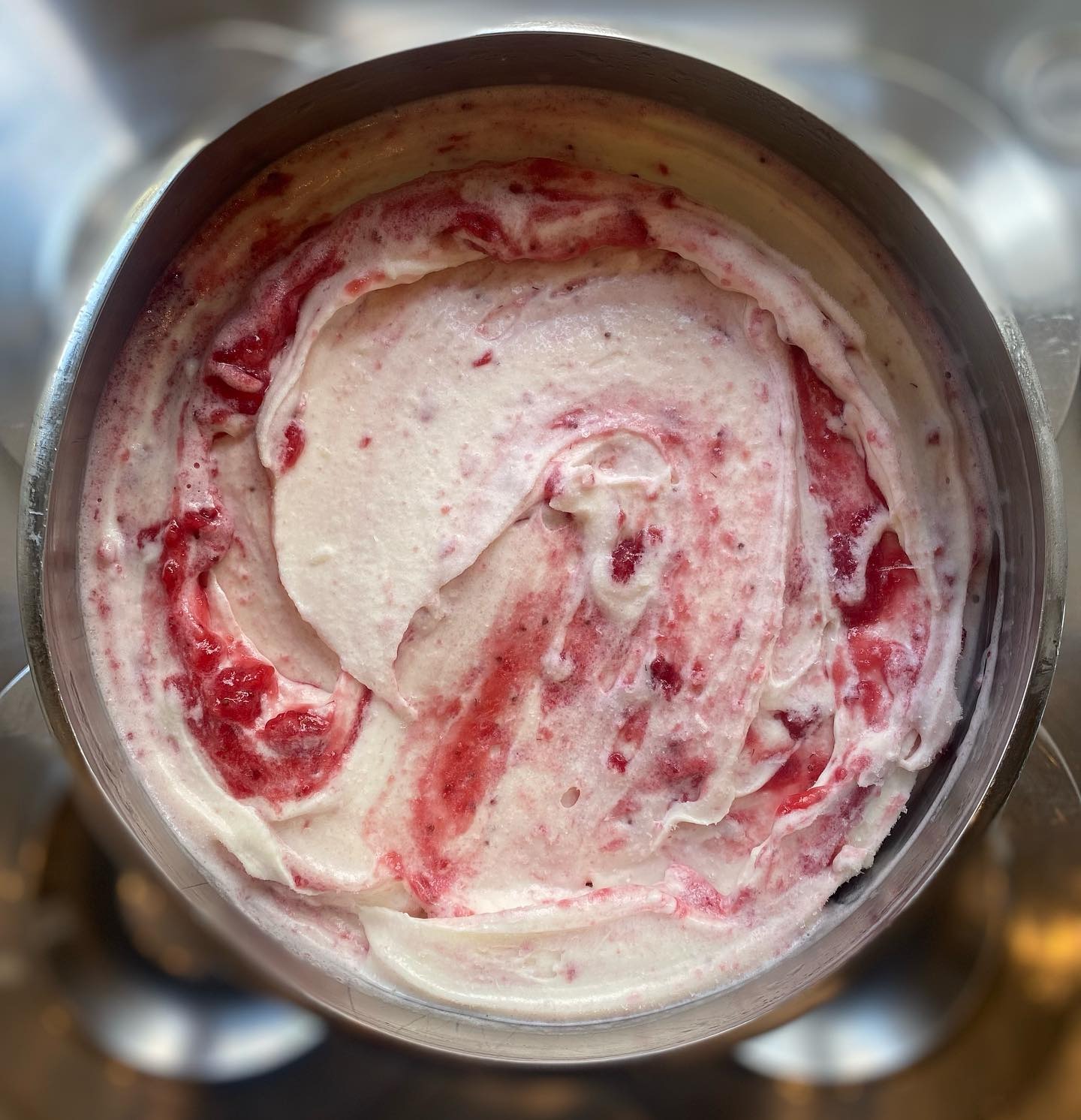 Metalowa patera wypełniona lodami o smaku śmietankowym i malinowym, z wyraźnymi smugami i kawałkami owoców, widok z góry.