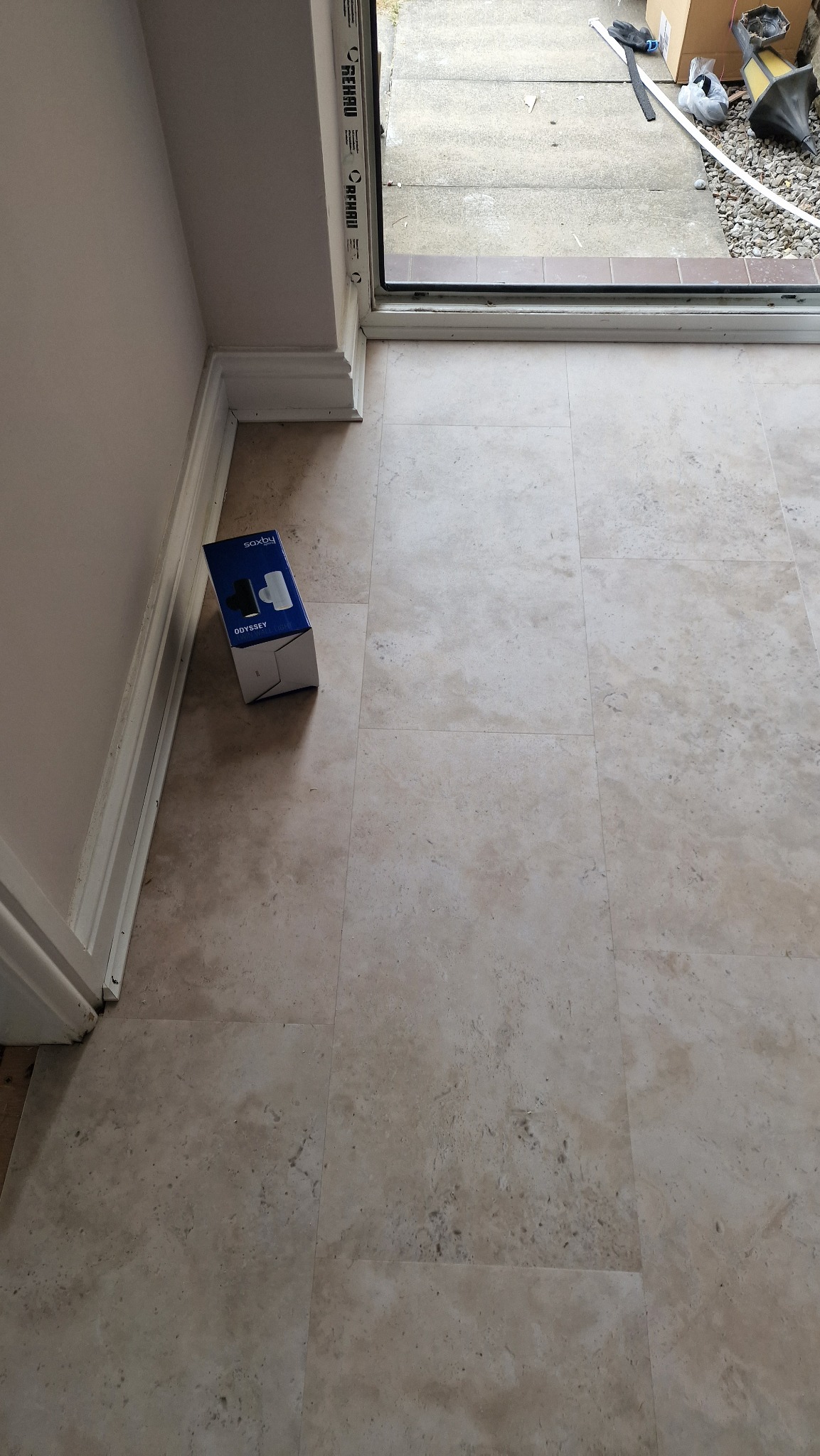 Ułożone beżowe panele podłogowe z widoczną paczką paneli przy ścianie i fragmentem progu drzwi wejściowych.