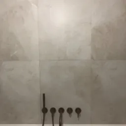 Wykończona łazienka z beżowymi płytkami imitującymi marmur i minimalistyczną armaturą w kolorze miedzi nad białą wanną.