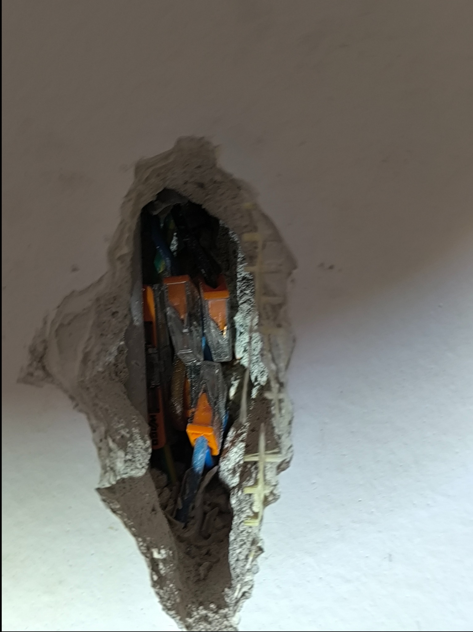 Otwór w ścianie z widocznymi przewodami elektrycznymi i złączkami Wago, surowy stan po kuciu.