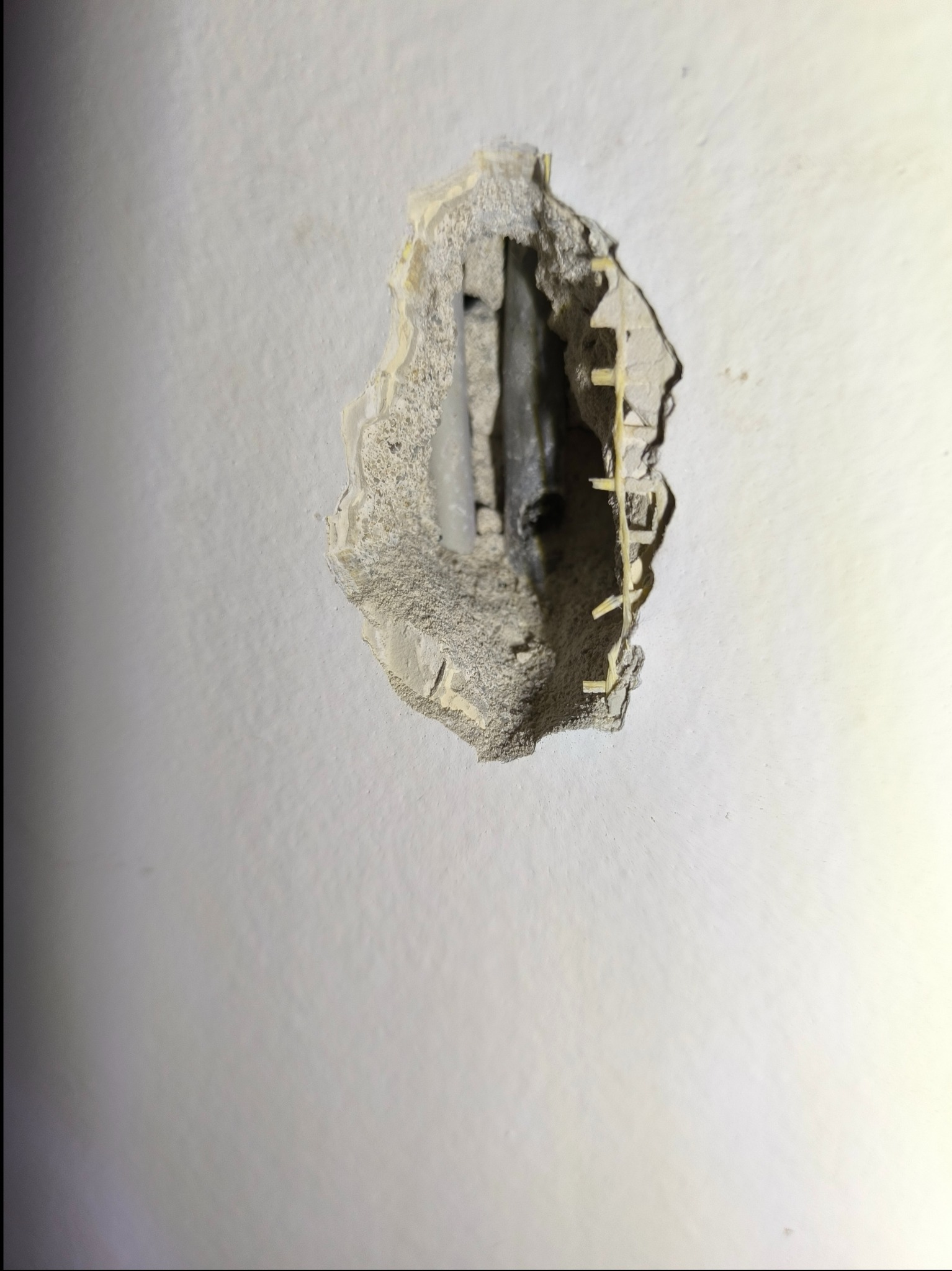 Uszkodzona ściana z widocznym przewodem elektrycznym i elementami mocującymi.