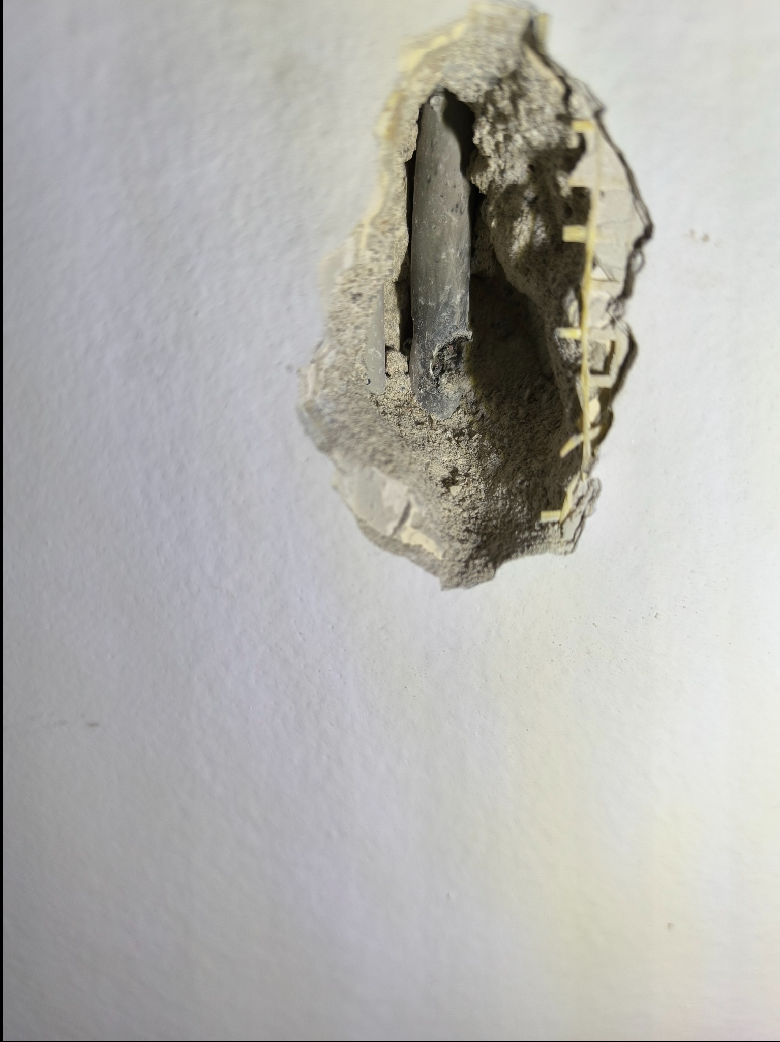 Przewód elektryczny wystający z dziury w ścianie, widoczne fragmenty uszkodzonego tynku i listwy montażowej.