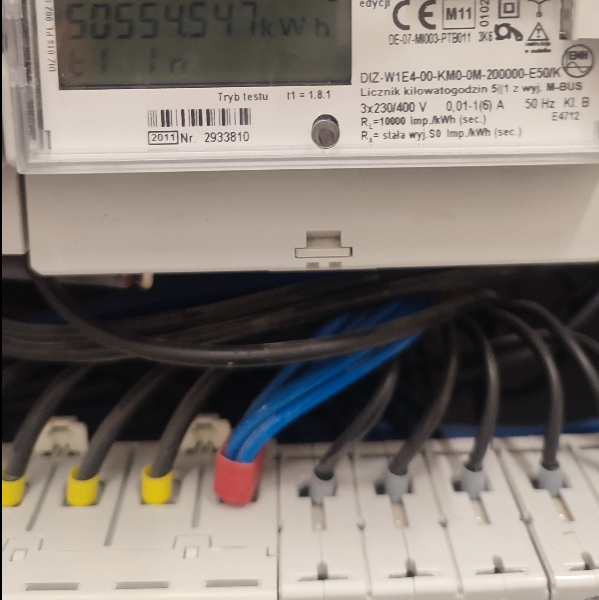Licznik energii elektrycznej z widocznymi przewodami podłączonymi do listwy zaciskowej, pokazujący odczyt 50554.547 kWh.