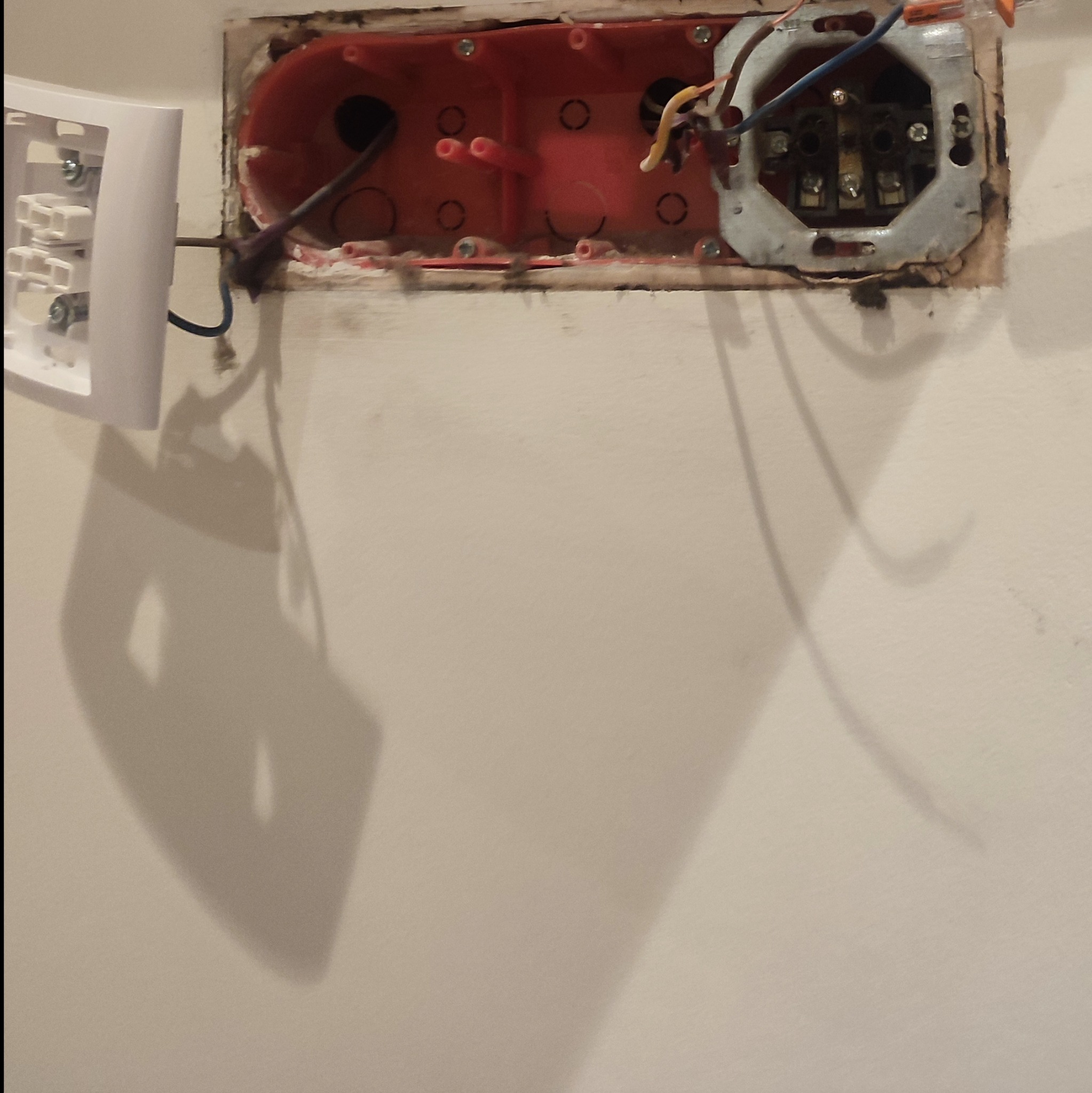 Otwarta puszka elektryczna w ścianie z widocznymi przewodami, obok zamontowany biały włącznik światła.