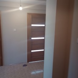 Grzegorz Kowalski - Wykończone wnętrze w Lututowie: pomalowane ściany w odcieniach beżu, drewniane drzwi z poziomymi przeszkleniami i ułożona podłoga z płytek ceramicznych.