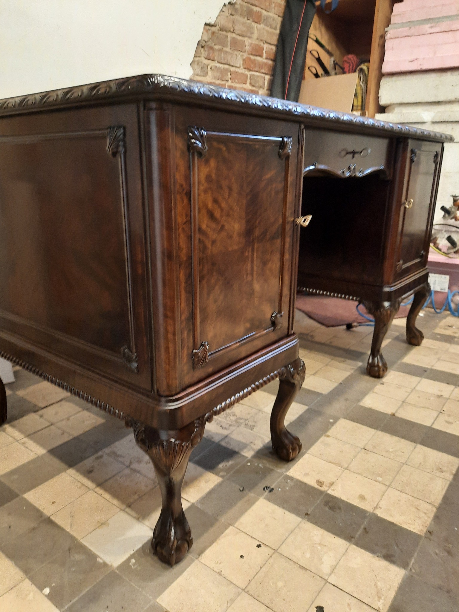 Antyczny, dwuczęściowy sekretarzyk z ciemnego drewna po renowacji, z widocznymi rzeźbionymi nogami w kształcie lwich łap i ornamentami roślinnymi na frontach, stojący na szachownicowej podłodze.