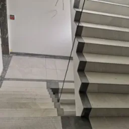 Wykończone schody z jasnych płytek z ciemnymi krawędziami, widok z góry, szklana balustrada, na podłodze płytki w tym samym stylu.