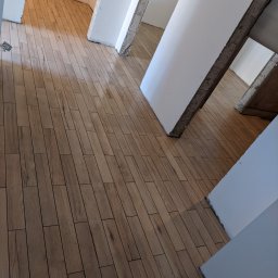 Marwit Vitalii Somushkin - Ułożona podłoga z płytek imitujących drewno w korytarzu, widoczne surowe wykończenia ścian i filarów.