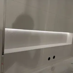 Wykończona ściana w łazience z białymi, falistymi płytkami, podświetlona wnęka i fragment wanny.