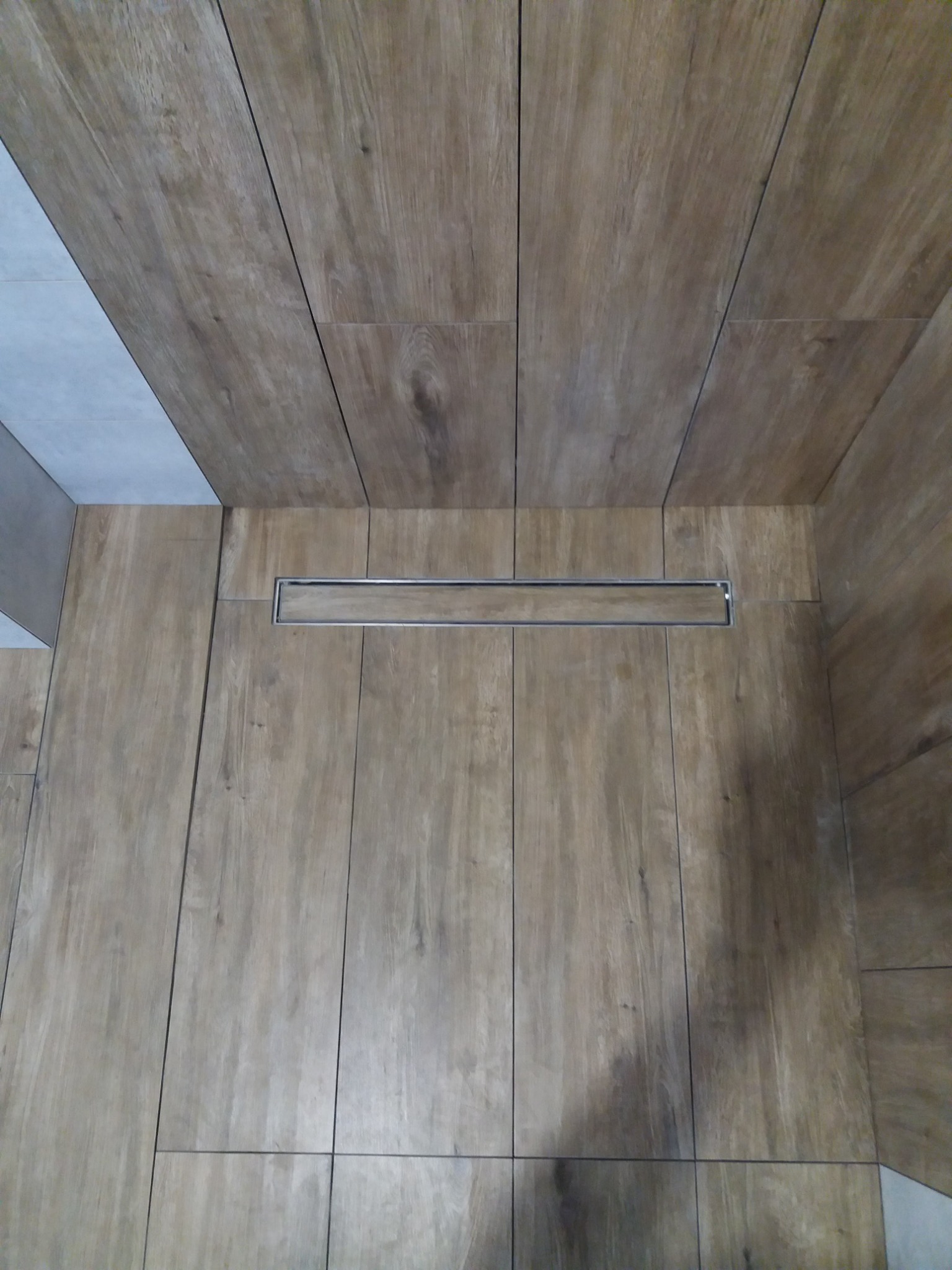 Wykończona kabina prysznicowa z odpływem liniowym i okładziną imitującą drewno, ułożoną pionowo na ścianach i podłodze.