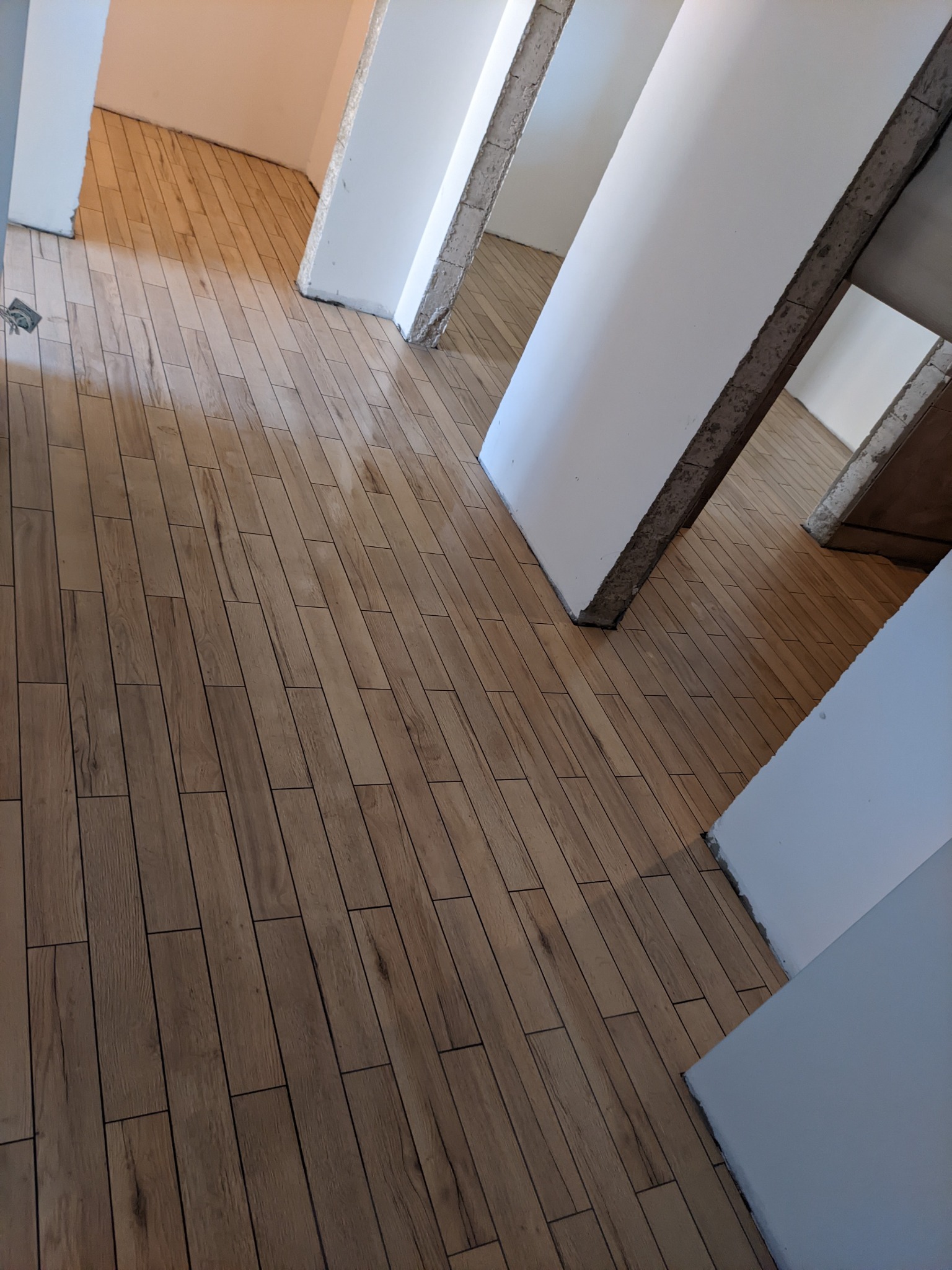 Ułożona podłoga z płytek imitujących drewno w korytarzu, widoczne surowe wykończenia ścian i filarów.