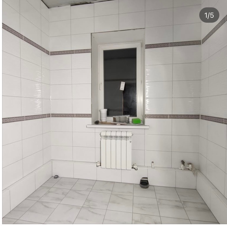 Biała łazienka z płytkami, dekoracyjny pas z motywem greckim, okno z parapetem, grzejnik. Widoczne narzędzia i akcesoria na parapecie. Podłoga wyłożona jasnymi płytkami.