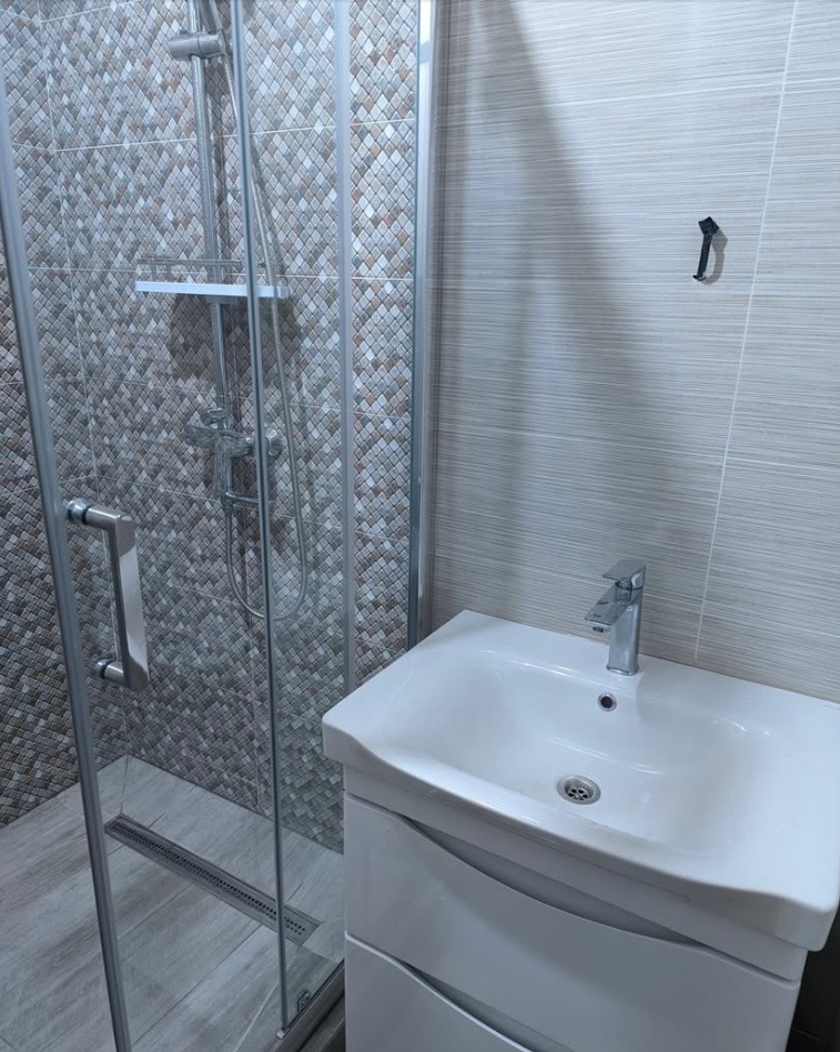 Nowoczesna łazienka z kabiną prysznicową w geometryczne wzory i białą umywalką z szafką. Minimalistyczny design, jasne płytki i chromowana armatura.