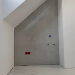 Ściana w łazience na poddaszu wyłożona szarymi płytkami imitującymi marmur, z widocznymi otworami na instalacje wodne i elektryczne, oraz biała podłoga z płytek o podobnym wzorze, oświetlona przez...