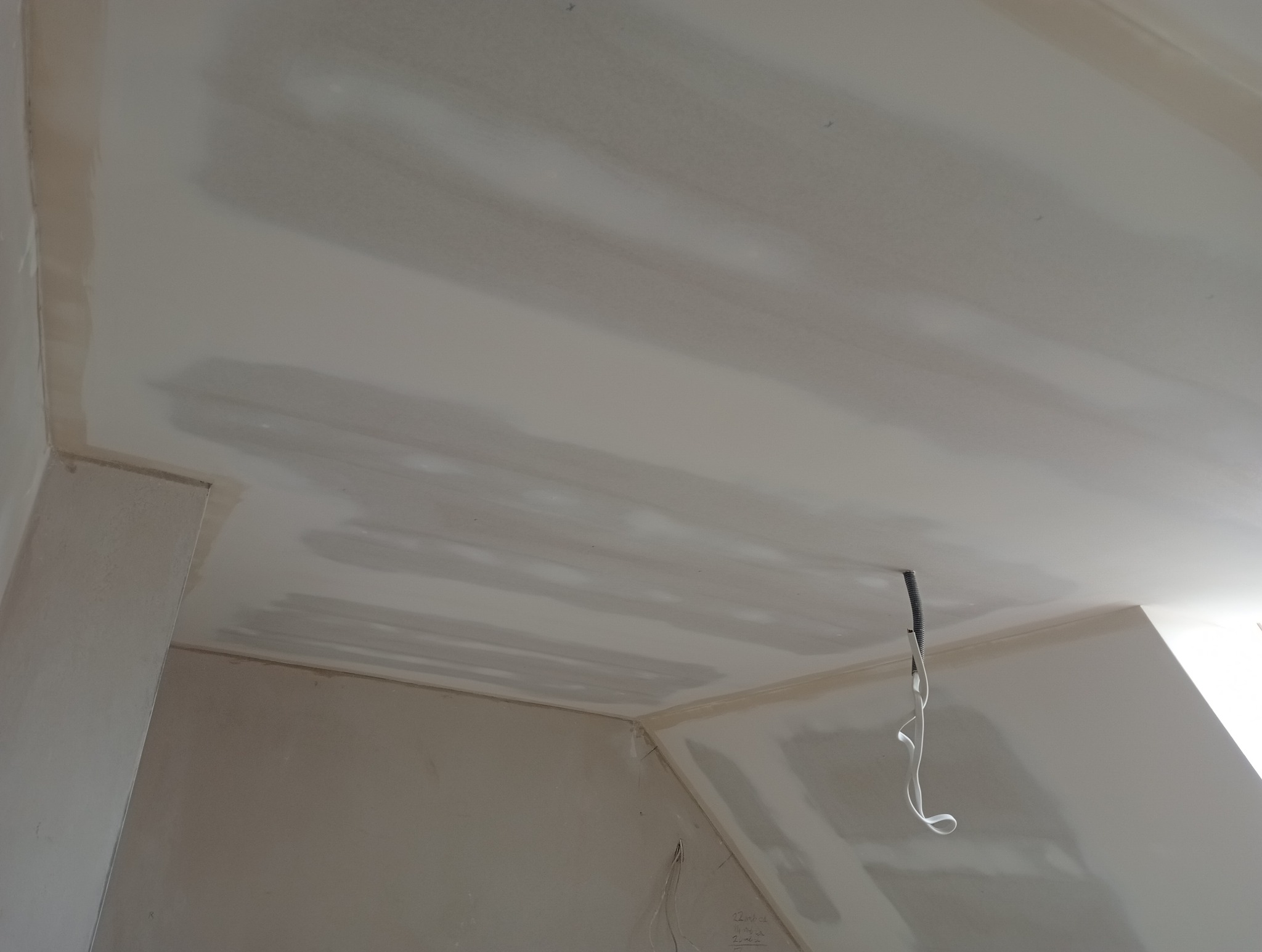 Wnętrze w trakcie prac wykończeniowych; widoczny sufit i ściany po szpachlowaniu, z widocznymi łączeniami płyt gipsowo-kartonowych i wystającym przewodem elektrycznym