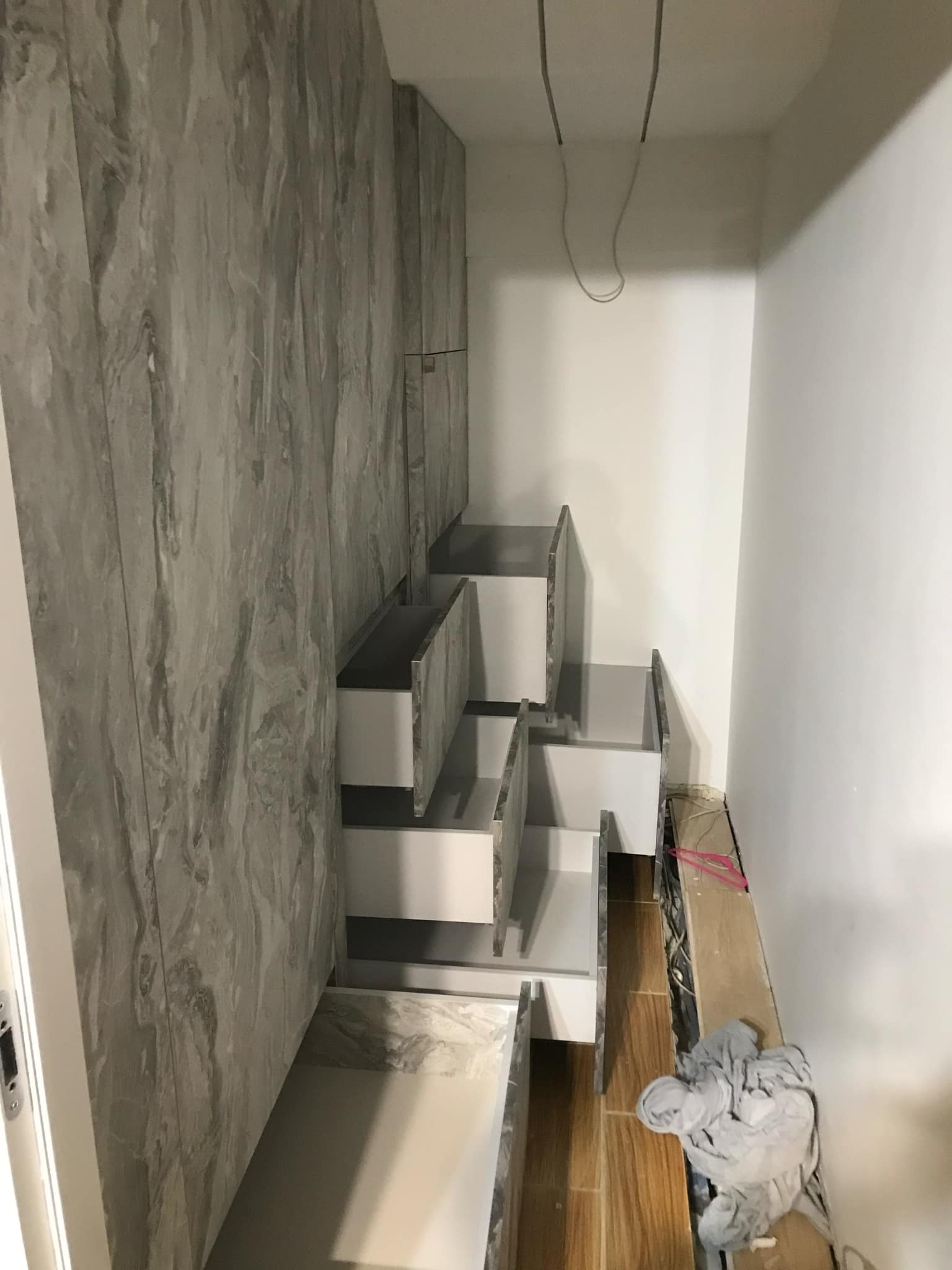 Szafa wnękowa na wymiar z szufladami, wykończona panelami imitującymi marmur, widoczna w trakcie montażu, z przewodami i drobnym bałaganem w tle.