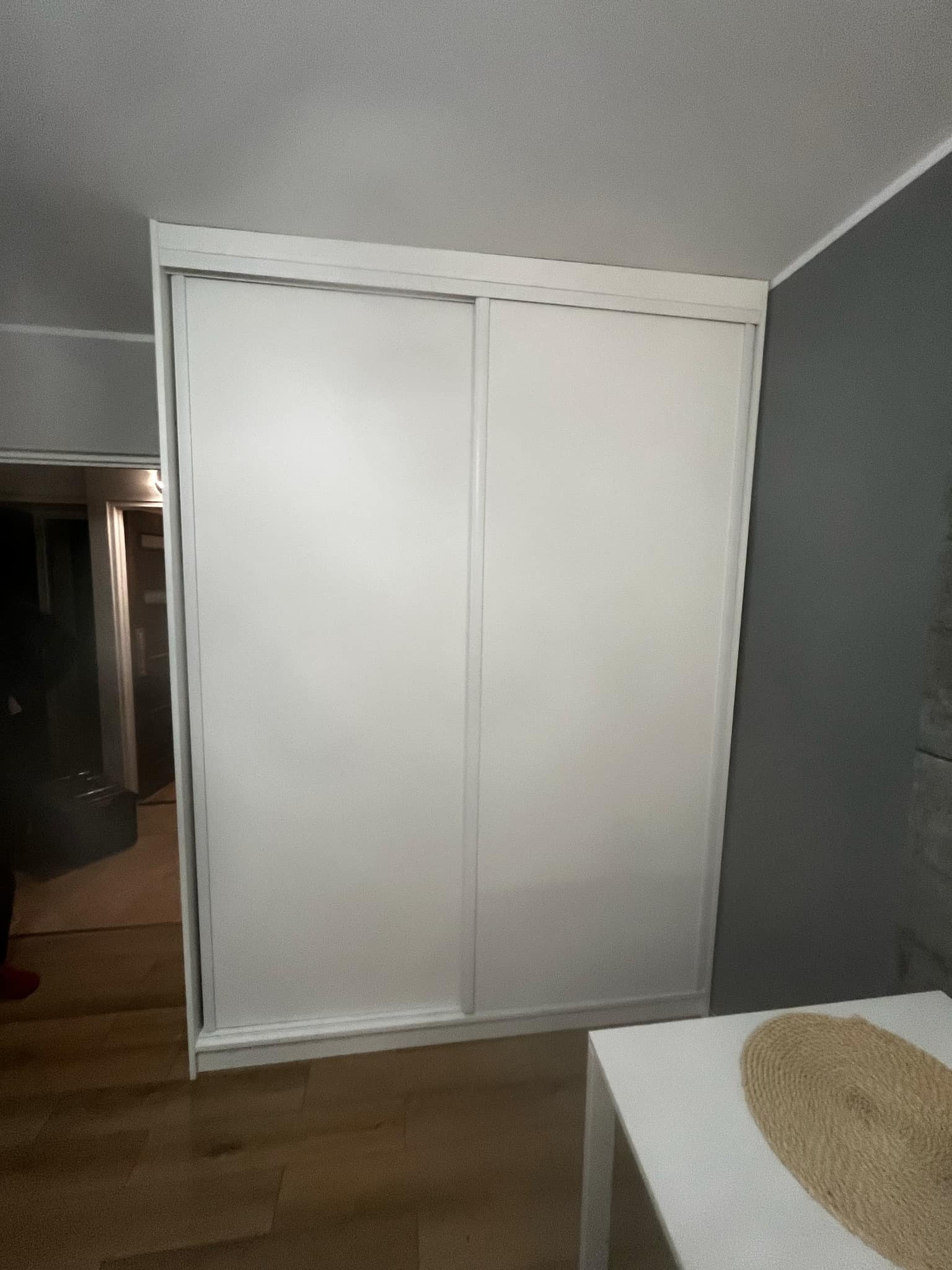 Biała szafa wnękowa z przesuwnymi drzwiami, zamontowana w mieszkaniu w Mosinie, widziana z boku, z fragmentem stołu w kadrze.