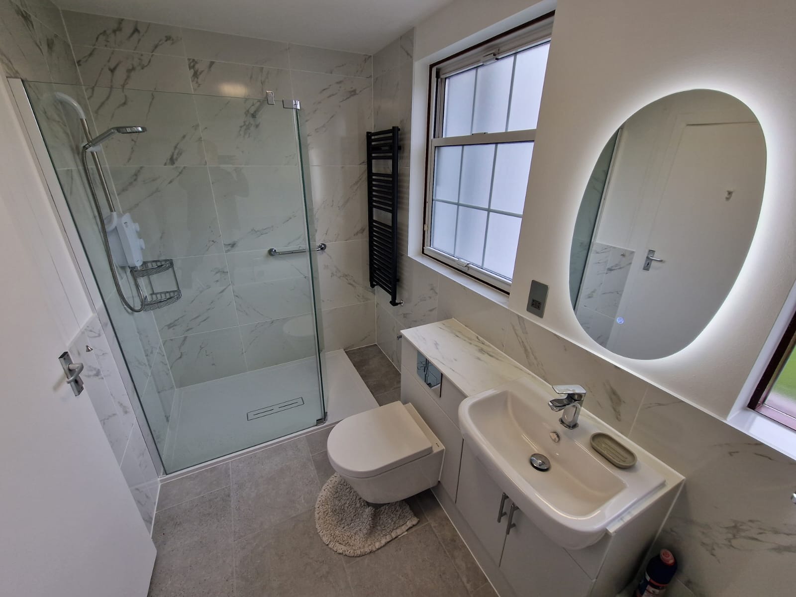 Nowoczesna łazienka z kabiną prysznicową typu walk-in, umywalką w zabudowie, podświetlanym lustrem i grzejnikiem drabinkowym, wykończona płytkami imitującymi marmur.