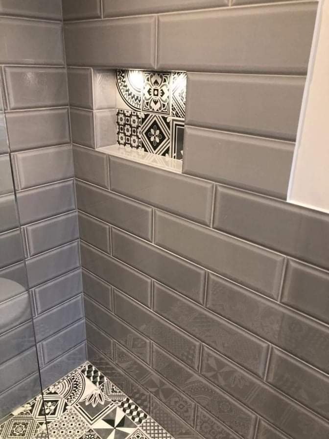 Szara łazienka z błyszczącymi, prostokątnymi płytkami ułożonymi horyzontalnie, dekoracyjna wnęka z podświetleniem i wzorzyste płytki podłogowe w stylu retro.