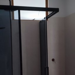 Termo Lux - Nowoczesna kabina prysznicowa z czarnymi profilami i jasnym oknem w tle, widoczna na tle jasnych ścian w trakcie wykańczania łazienki.