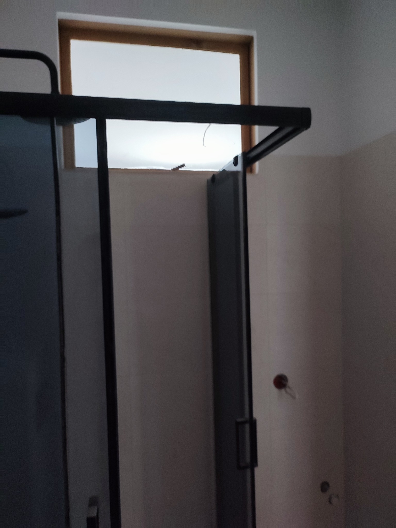 Nowoczesna kabina prysznicowa z czarnymi profilami i jasnym oknem w tle, widoczna na tle jasnych ścian w trakcie wykańczania łazienki.