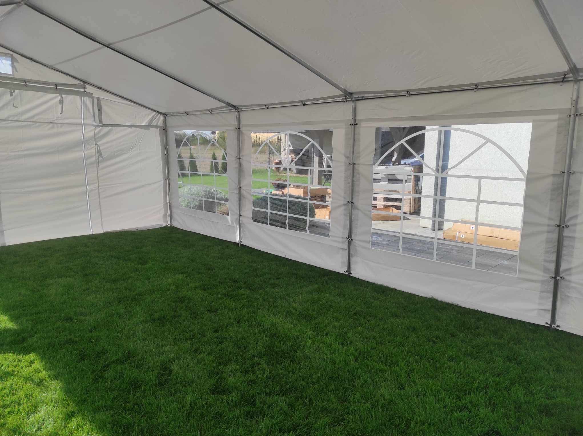 Wnętrze białego namiotu z widokiem na zewnątrz przez okna z siatką. Podłoga wyłożona zieloną trawą.