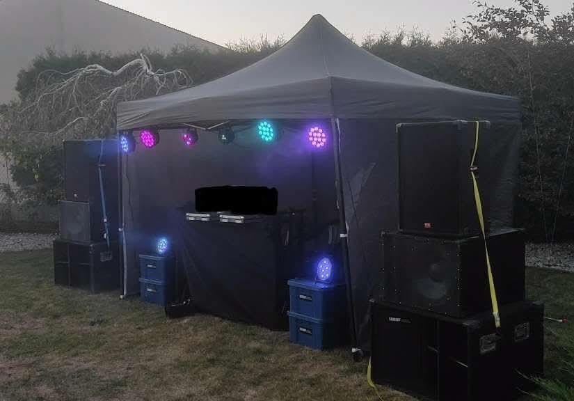 Czarny namiot z nagłośnieniem i oświetleniem LED na trawie. Kolorowe światła tworzą imprezowy klimat. Scena gotowa na występ.