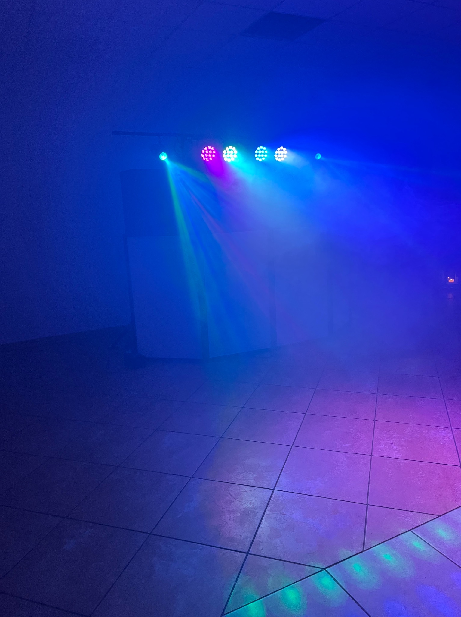 Oświetlenie sceniczne z reflektorami w kolorach: niebieskim, zielonym i różowym, skierowane na parkiet w zadymionym pomieszczeniu. Efekt wizualny dla imprez.