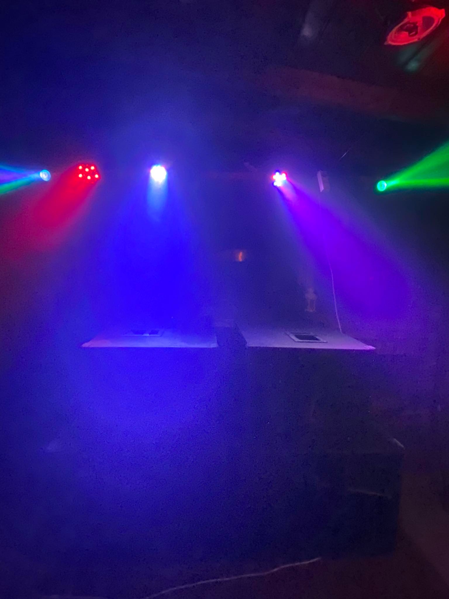 Scena oświetlona kolorowymi światłami, z dwoma białymi podestami na pierwszym planie, oświetlonymi niebieskim światłem.