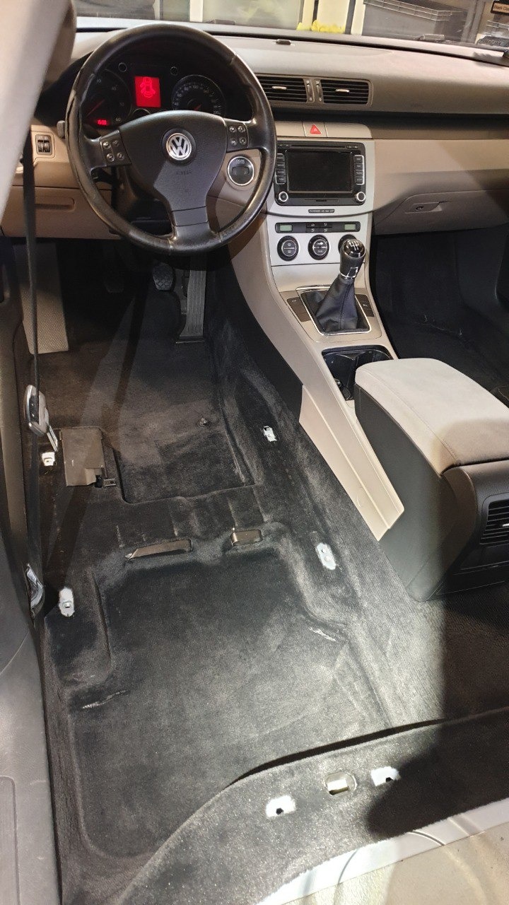 Wnętrze samochodu Volkswagen Passat z widoczną podłogą w trakcie czyszczenia, zdemontowane elementy wykończenia, widoczna kierownica, deska rozdzielcza i konsola środkowa.