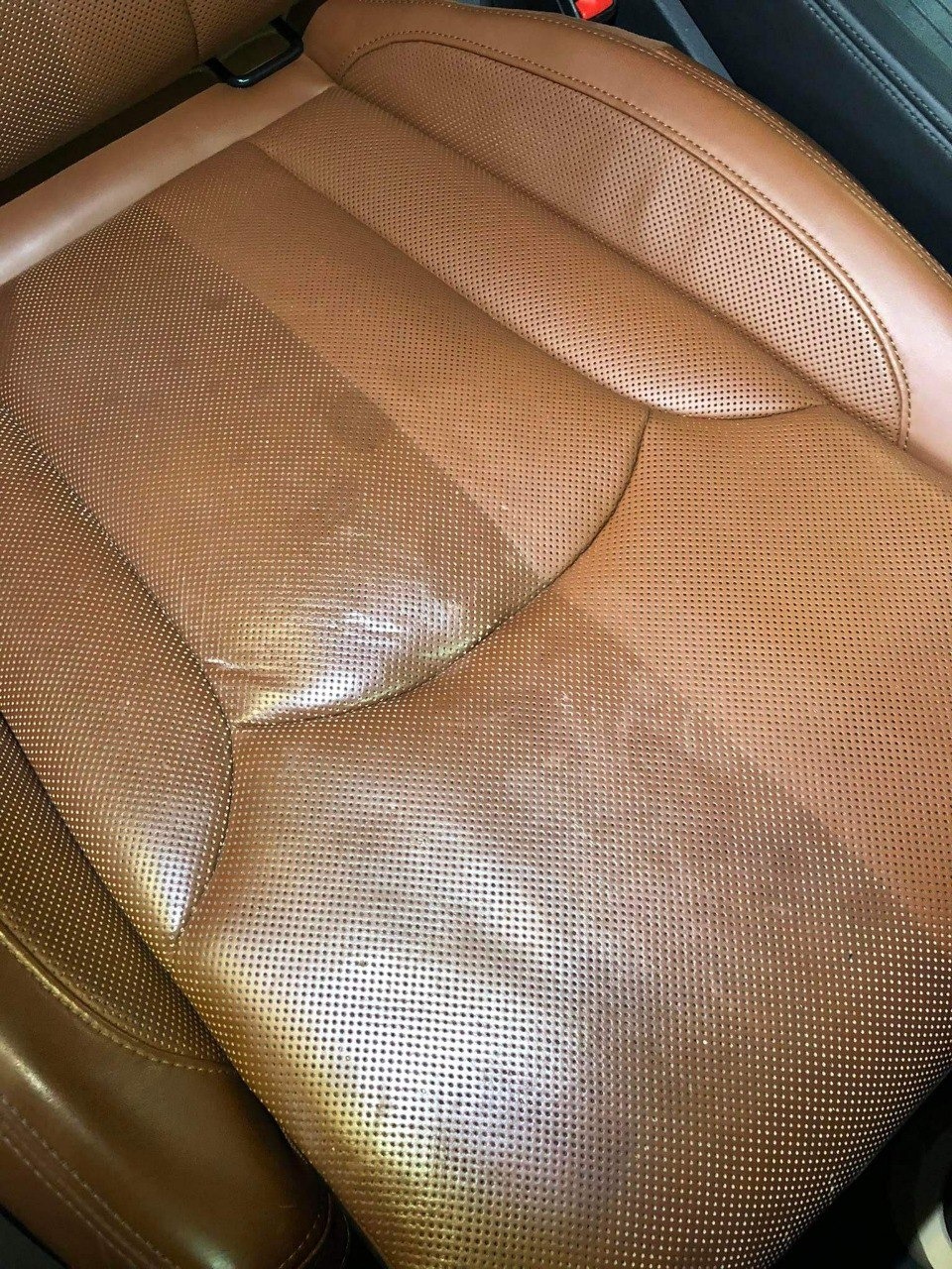 Brązowe, perforowane skórzane siedzenie samochodowe, częściowo wyczyszczone, ukazujące różnicę w wyglądzie przed i po czyszczeniu.