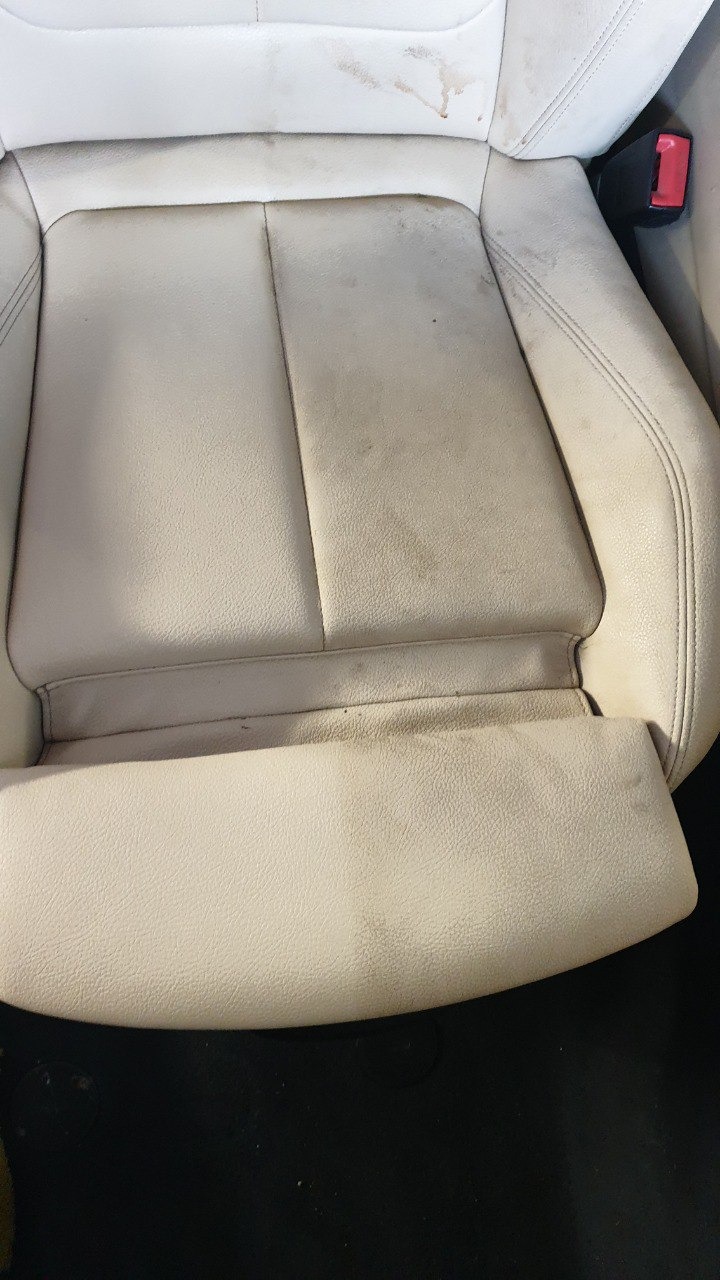 Bardzo brudne, jasne skórzane siedzenie samochodowe z widocznymi plamami i zabrudzeniami na całej powierzchni.