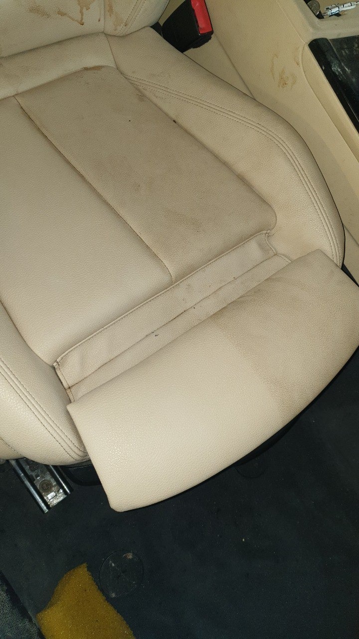 Beżowe skórzane siedzenie samochodowe z widocznymi plamami i zabrudzeniami, wymagające czyszczenia tapicerki.